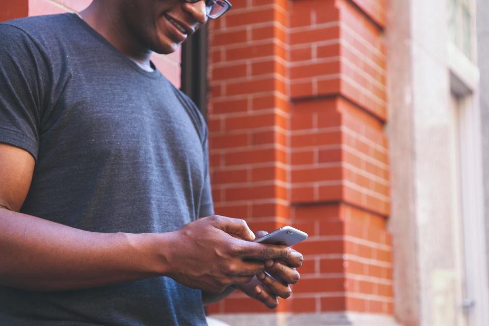 Cidadão sorrindo ao olhar o celular em meio aos prédios da cidade